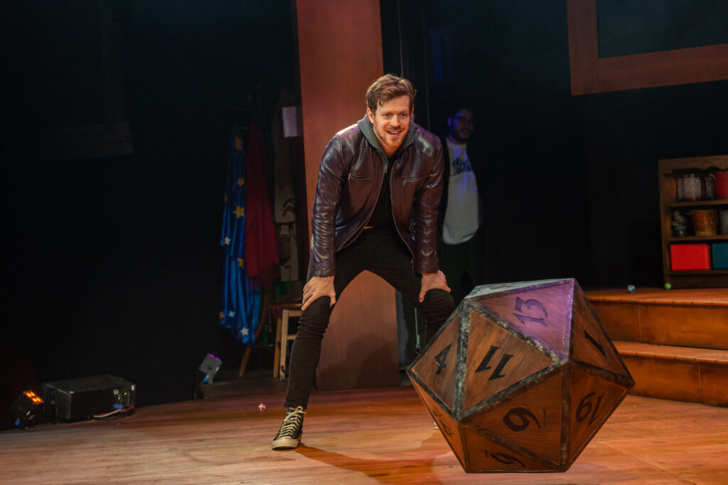 A man in a leather jacket rolls an oversized die