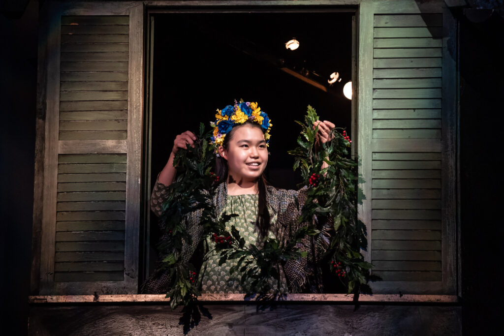 A child in a flower crown holds up a garland